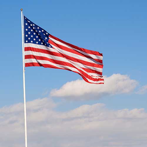 Nylon American Flag - Beacon® flying on a tall white flagpole against a clear blue sky with scattered clouds.