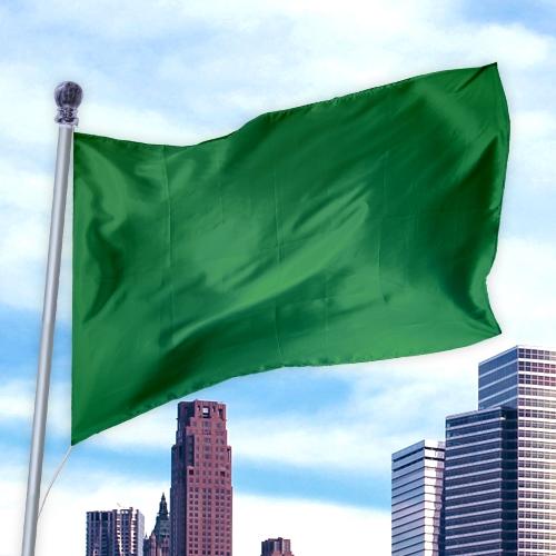 Green solid colored flag made of durable nylon flying on a pole above a cityscape, Solid Colored Flags - Premier Nylon.