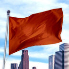 Bright solid red flag made from durable Premier Nylon waving on a silver pole against a city skyline background, Solid Colored Flags - Premier Nylon.