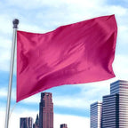 Bright solid magenta flag made from durable premier nylon material flying on a pole against a city skyline background with blue sky, representing Solid Colored Flags - Premier Nylon.