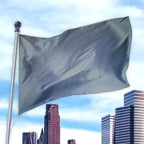 Gray flag made of nylon fabric flying on a pole above a city skyline, Solid Colored Flags - Premier Nylon.