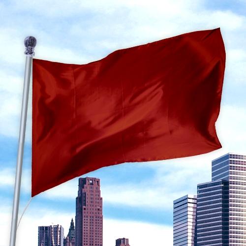 Red flag made of durable nylon fabric flying on a pole against a city skyline, showcasing Solid Colored Flags - Premier Nylon.