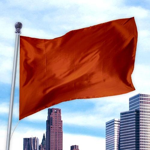 Red solid colored flag made of durable nylon waving on a pole against a city skyline backdrop, Solid Colored Flags - Premier Nylon.