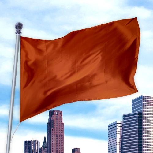 Solid Colored Flags - Premier Nylon in burnt orange waving on a flagpole against a city skyline and blue sky background