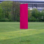 Solid Tall Advertising Flags with a vibrant magenta banner standing upright on a metal pole in a grassy outdoor area near trees and a stadium.