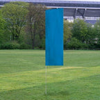Solid Tall Advertising Flags in a solid blue color displayed outdoors on a grassy field with trees and a stadium structure in the background.