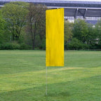 Solid Tall Advertising Flags in bright yellow standing on a grassy field with trees and a stadium in the background.