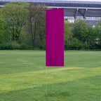 Solid Tall Advertising Flags in a solid magenta color displayed upright on a grassy field with trees and a building in the background.