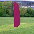 Solid Color Feather Flags in magenta standing on a grassy field with trees and a stadium in the background