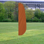 Solid Color Feather Flags in orange displayed outdoors on a grassy field with trees and a stadium in the background.