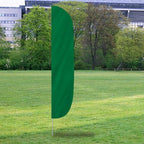Solid Color Flutter Flags in green displayed outdoors on a grassy field with trees and buildings in the background.