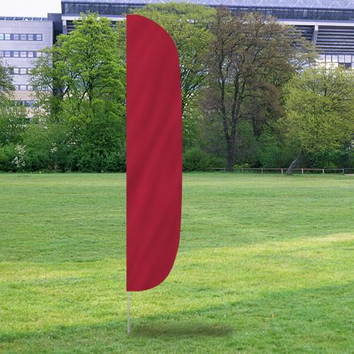 Solid Color Flutter Flags in a solid red shade standing upright on a grassy field with trees and buildings in the background