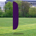 Solid Color Flutter Flags in deep purple displayed outdoors on a grassy field with trees and buildings in the background.