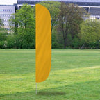 Solid Color Flutter Flags in bright yellow standing on a grassy field with trees and modern buildings in the background