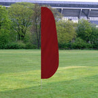 Solid Color Feather Flags in deep red displayed outdoors on a grassy field with trees and a stadium in the background.