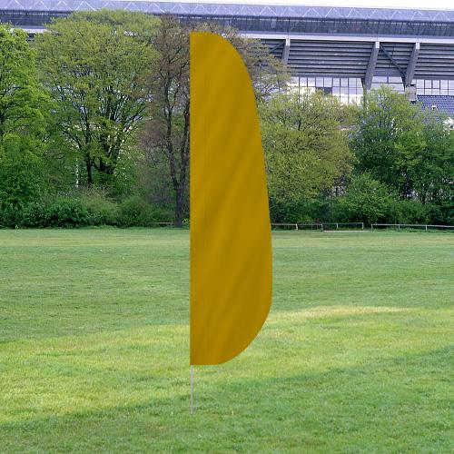 Solid Color Feather Flags in yellow standing upright on a grassy field with trees and a stadium structure in the background.