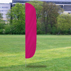 Magenta Solid Color Flutter Flags standing on a grassy field with trees and buildings in the background.
