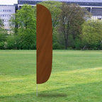 A brown Solid Color Flutter Flags banner standing upright on a grassy area with trees and buildings in the background.